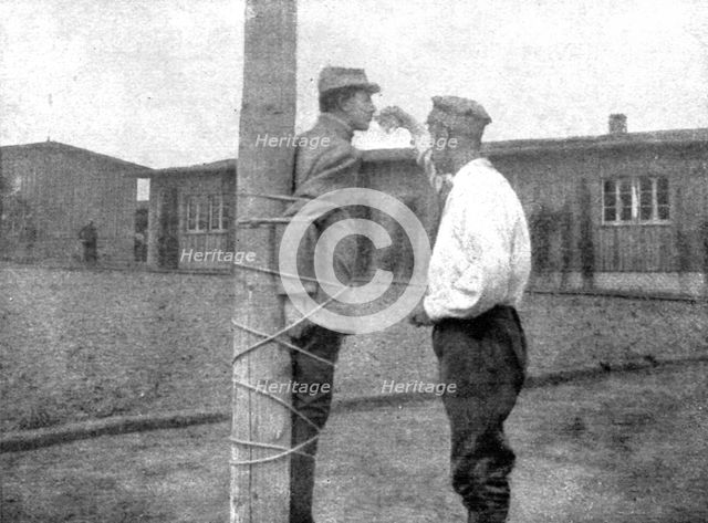 'La peine du poteau; a Zwickau: un Francais, lie au poteau, recoit d'un prisonnier roumain..., 1917. Creator: Unknown.