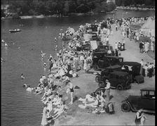 Large Group of People Sitting by a Riverside with Cars, 1933. Creator: British Pathe Ltd