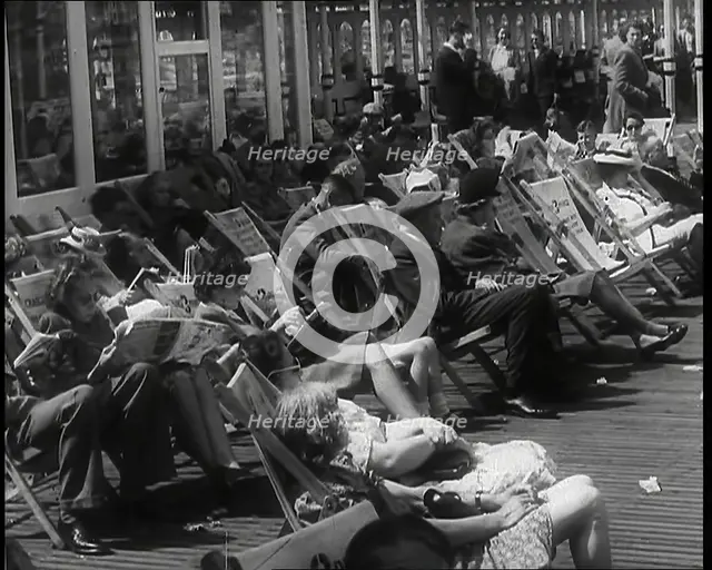 Lines of Men and Women Sitting in Deckchairs on a Pier at  Brighton With Several Reading..., 1939. Creator: British Pathe Ltd.