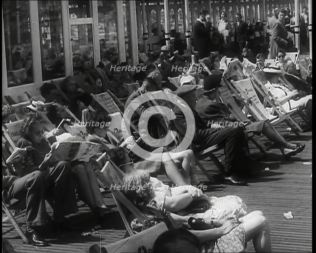 Lines of Men and Women Sitting in Deckchairs on a Pier at  Brighton With Several Reading..., 1939. Creator: British Pathe Ltd.