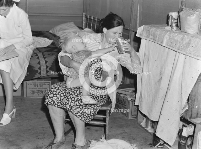 Mother from Oklahoma tends baby with dysentery, FSA camp, Tulare County, California, 1939. Creator: Dorothea Lange.