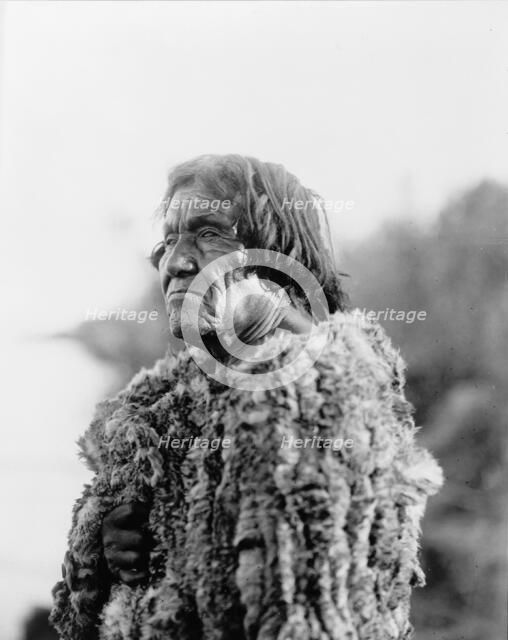 Mohave man, half-length portrait, facing left wearing "primitive" robe of rabbit skin, 1907. Creator: Edward Sheriff Curtis.