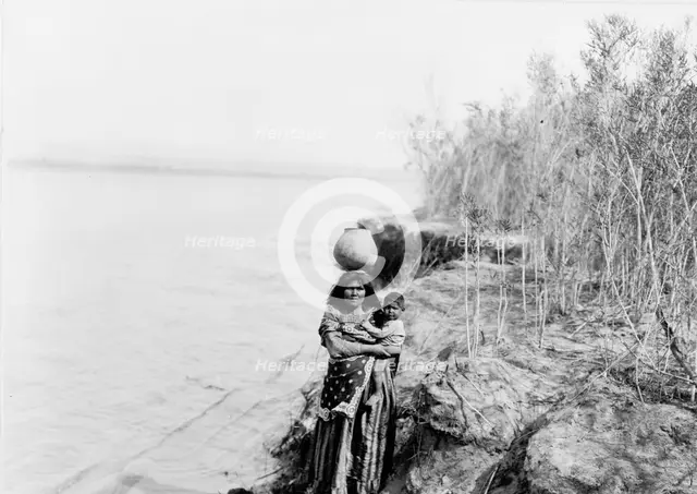 Mohave woman carrying water on her head and holding child, c1903. Creator: Edward Sheriff Curtis.