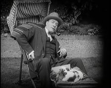 Matheson Lang Relaxing in a Deck Chair Smoking a Pipe With a Dog at His Feet, 1920s. Creator: British Pathe Ltd