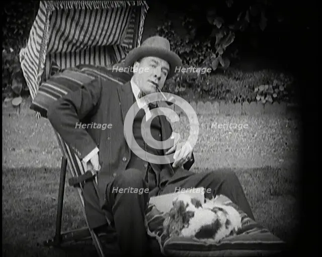 Matheson Lang Relaxing in a Deck Chair Smoking a Pipe With a Dog at His Feet, 1920s. Creator: British Pathe Ltd.