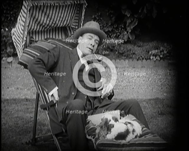 Matheson Lang Relaxing in a Deck Chair Smoking a Pipe With a Dog at His Feet, 1920s. Creator: British Pathe Ltd.