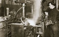 Making money; lowering a pot of liquid metal into a machine, 20th century