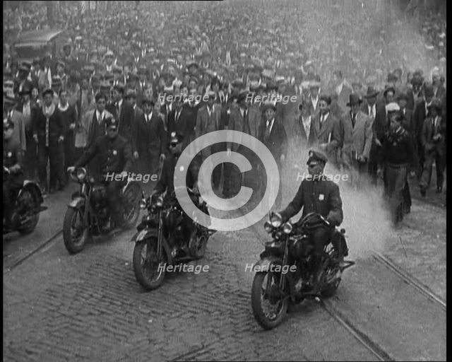 Male American Police Officers Riding Motorbikes Escorting a Large Crowd in a Parade, 1930. Creator: British Pathe Ltd.