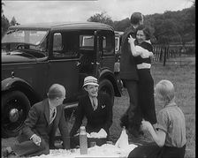 Male and Female Civilians Having a Picnic Beside a Car Whilst Two of Them Are Dancing, 1931. Creator: British Pathe Ltd