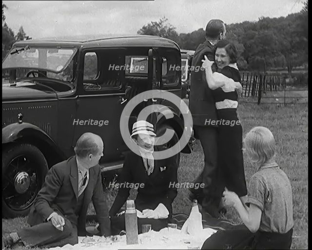 Male and Female Civilians Having a Picnic Beside a Car Whilst Two of Them Are Dancing, 1931. Creator: British Pathe Ltd.