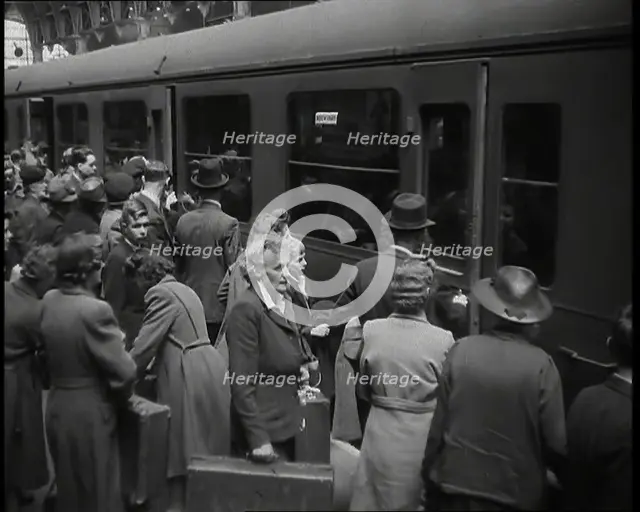 Male and Female Passengers, Some Holding Suitcases, on a Platform of a Large Train Station..., 1938. Creator: British Pathe Ltd.