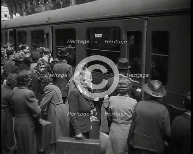 Male and Female Passengers, Some Holding Suitcases, on a Platform of a Large Train Station..., 1938. Creator: British Pathe Ltd.