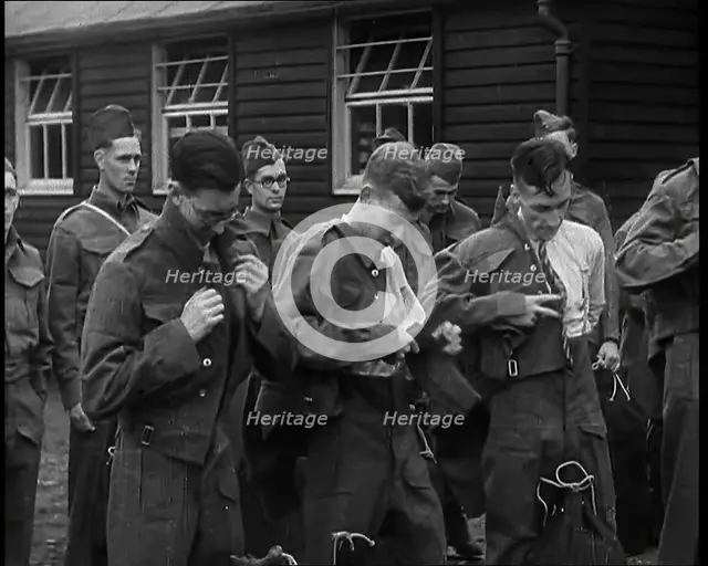 Male British Soldiers Putting on The Tunics of Their Uniforms in Front of Wooden Hut, 1939. Creator: British Pathe Ltd.
