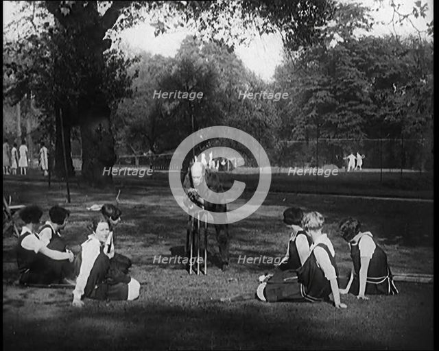 Male Civilian Demonstrating How to Set up a Cricket Wicket to a Group of Young Female..., 1920. Creator: British Pathe Ltd.
