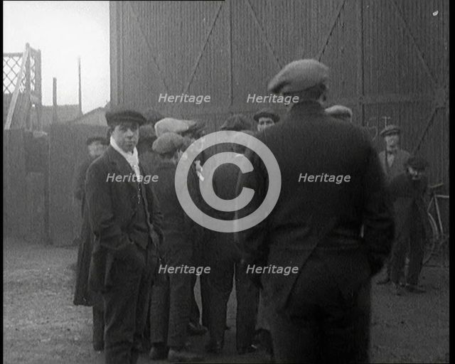 Male Civilian in a Flat Cap Facing a Wall. Another Male Civilian Carries a Sack Over His..., 1924. Creator: British Pathe Ltd.