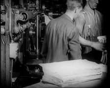 Male Printers Pulling Newspapers Off the Printing Press, 1921. Creator: British Pathe Ltd