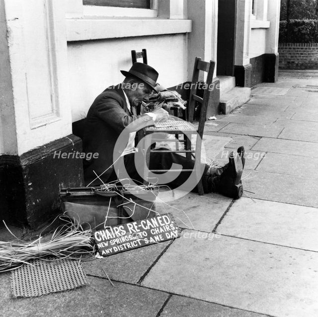 Man mending a chair on an East End street, London, 1950s. Creator: Henry Grant.