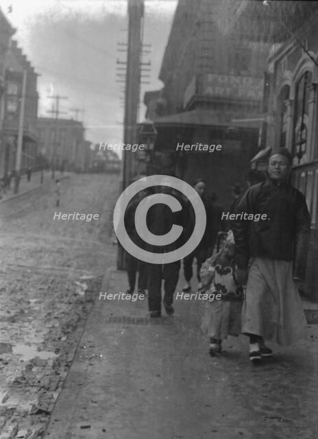 Man and a boy walking down a sidewalk with other people, Chinatown, San Francisco, c1896-1906. Creator: Arnold Genthe.