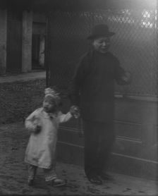 Man and a young child walking down a street, Chinatown, San Francisco, between 1896 and 1906. Creator: Arnold Genthe