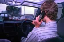 Man driving whilst using built-in car telephone 1990. Creator: Unknown