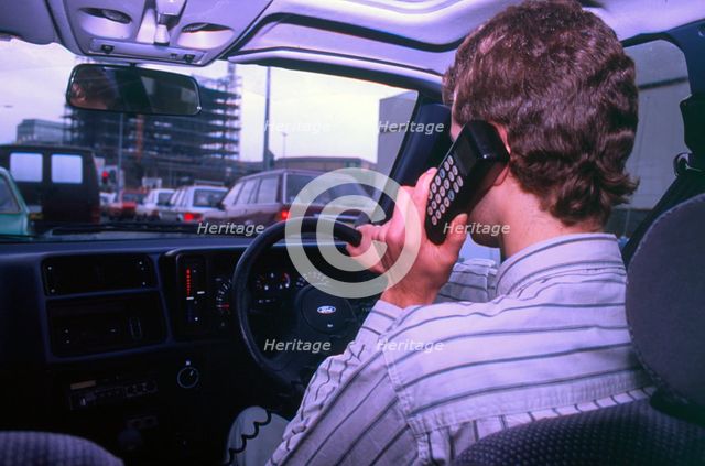 Man driving whilst using built-in car telephone 1990. Creator: Unknown.