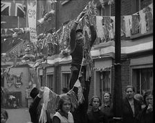 Man Hanging Bunting from a Lamp Post in a Street With Decorations For the Coronation of..., 1937. Creator: British Pathe Ltd