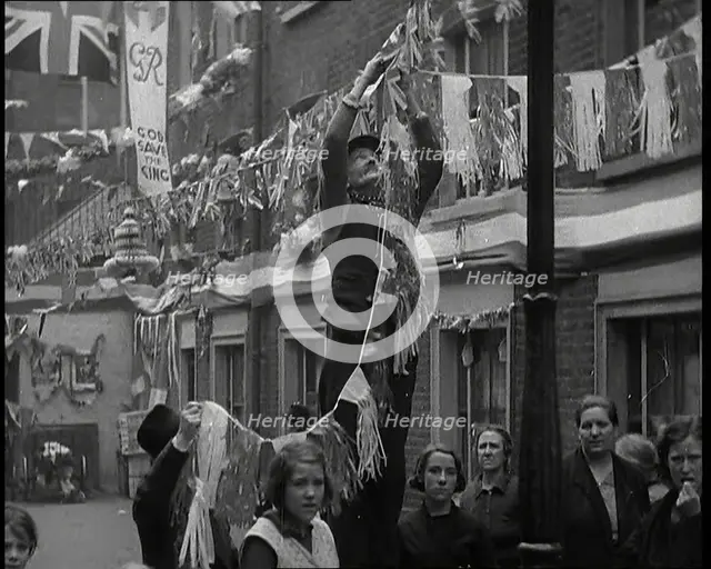 Man Hanging Bunting from a Lamp Post in a Street With Decorations For the Coronation of..., 1937. Creator: British Pathe Ltd.