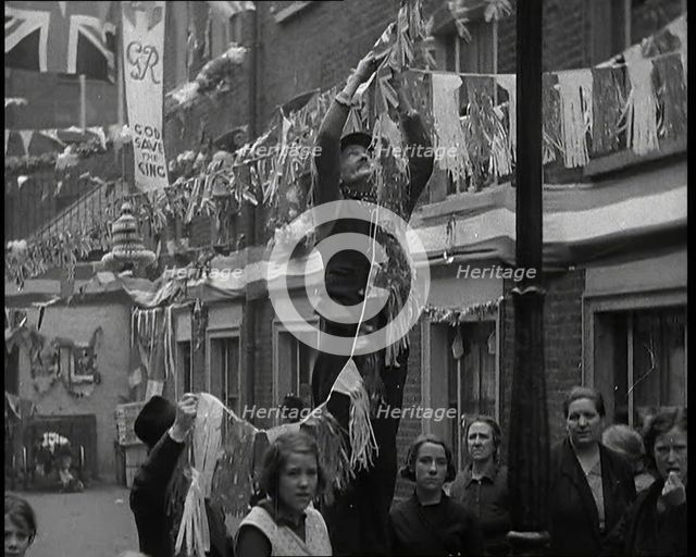 Man Hanging Bunting from a Lamp Post in a Street With Decorations For the Coronation of..., 1937. Creator: British Pathe Ltd.