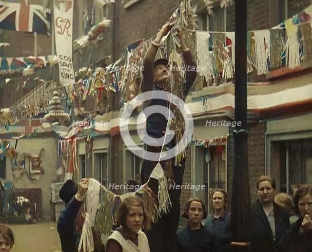 Man Hanging Bunting from a Lamp Post in a Street With Decorations For the Coronation of..., 1937. Creator: British Pathe Ltd.