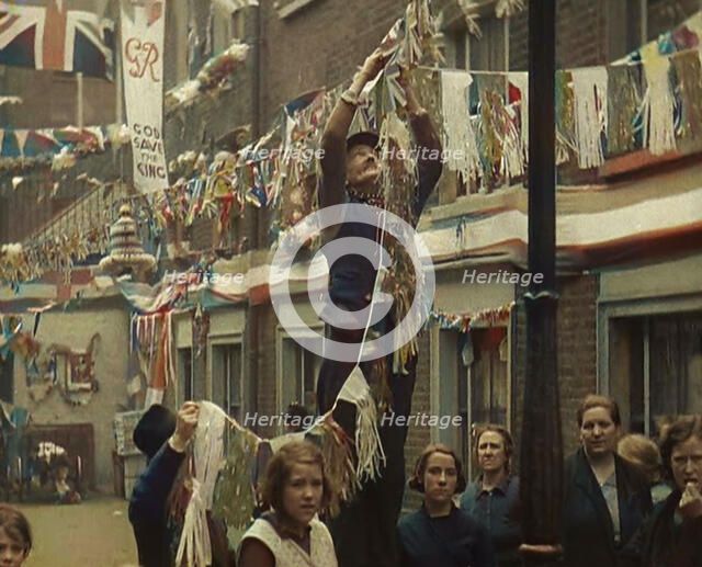Man Hanging Bunting from a Lamp Post in a Street With Decorations For the Coronation of..., 1937. Creator: British Pathe Ltd.