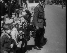 Man in Uniform Helping Young Children Cross the Road, 1933. Creator: British Pathe Ltd