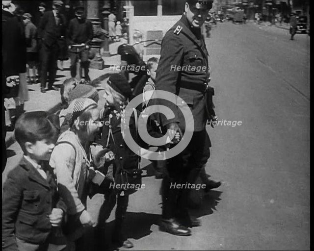Man in Uniform Helping Young Children Cross the Road, 1933. Creator: British Pathe Ltd.