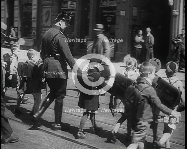 Man in Uniform Helping Young Children Cross the Road, 1933. Creator: British Pathe Ltd.