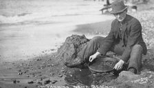 Man panning gold on Nome Beach, between c1900 and c1930. Creator: Lomen Brothers