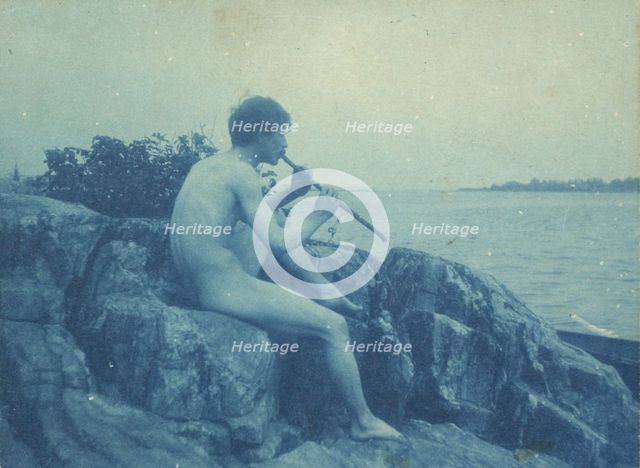 Man posed on rocks, nude, playing pipe (Pan), between 1885 and 1900. Creator: Frances Benjamin Johnston.