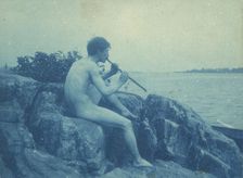 Man posed on rocks, nude, playing pipe (Pan), between 1885 and 1900. Creator: Frances Benjamin Johnston