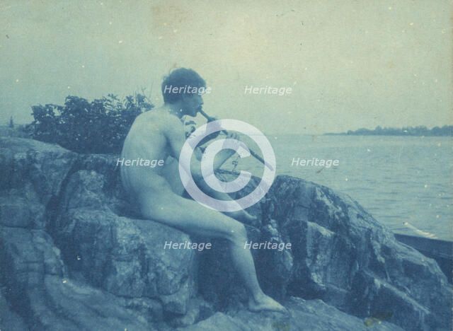 Man posed on rocks, nude, playing pipe (Pan), between 1885 and 1900. Creator: Frances Benjamin Johnston.