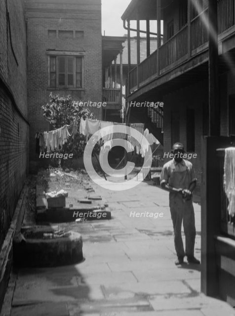 Man standing in a courtyard, New Orleans, between 1920 and 1926. Creator: Arnold Genthe.