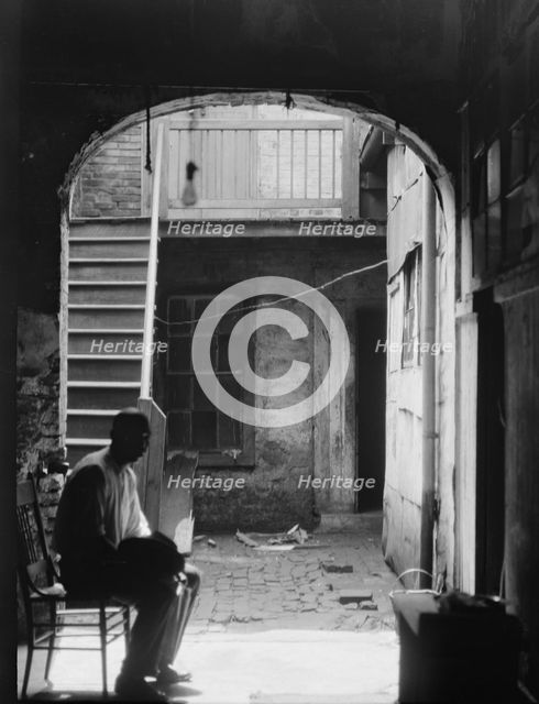 Man seated in archway leading to a courtyard, New Orleans, between 1920 and 1926. Creator: Arnold Genthe.