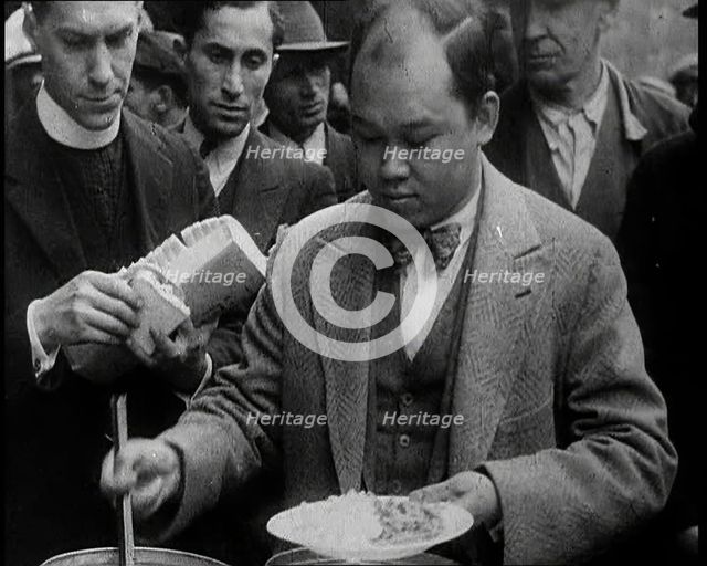 Man Serving Meals For Group of People from the Street Kitchen, 1932. Creator: British Pathe Ltd.
