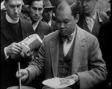 Man Serving Meals For Group of People from the Street Kitchen, 1932. Creator: British Pathe Ltd