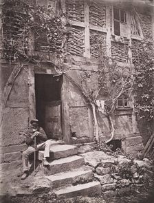[Man Sitting on Steps of House with Socks Hanging on Nearby Vine to Dry], 1880s. Creator: Unknown