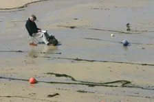 Man sitting on the sand in St Ives harbour at low tide, Cornwall. Creator: Peter Thompson