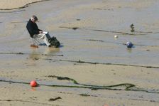 Man sitting on the sand in St Ives harbour at low tide, Cornwall. Creator: Peter Thompson