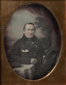 Man Wearing Coat and Gloves, Holding Hat, Seated in Front of Painted Outdoor Backdrop, 1840s. Creator: Attributed to Samuel Broadbent Jr.