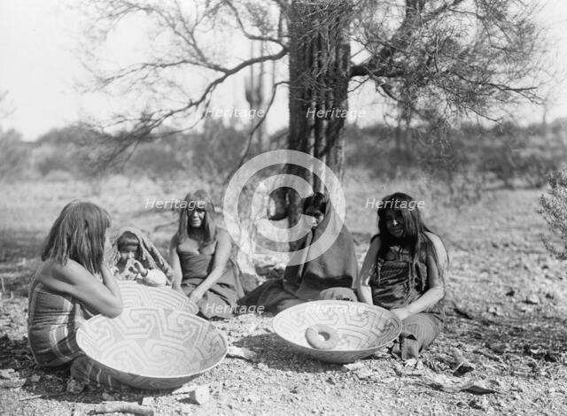 Maricopa group, Arizona. Four women and a child seated on ground with three large basket trays,c1907 Creator: Edward Sheriff Curtis.
