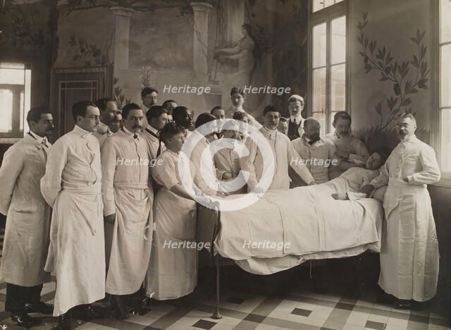 Medical staff standing round a woman patient in bed in a hospital ward, c1910. Creator: Freres Seeberger.