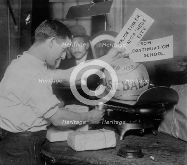 Medicine ball being weighed by Post Office employee; shipping tags read: Mr. Joe Tinker..., 1913. Creator: Bain News Service.