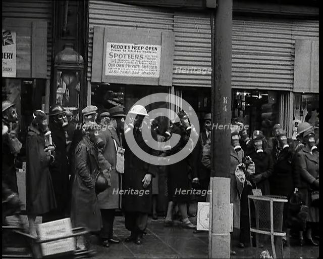 Men and Women Waiting on a Pavement Wearing Gas Masks, 1939. Creator: British Pathe Ltd.