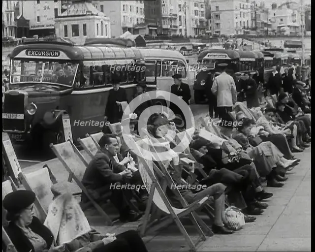 Men and Women Sitting in Deckchairs on the Promenade at  Brighton With a Row of Buses..., 1939. Creator: British Pathe Ltd.
